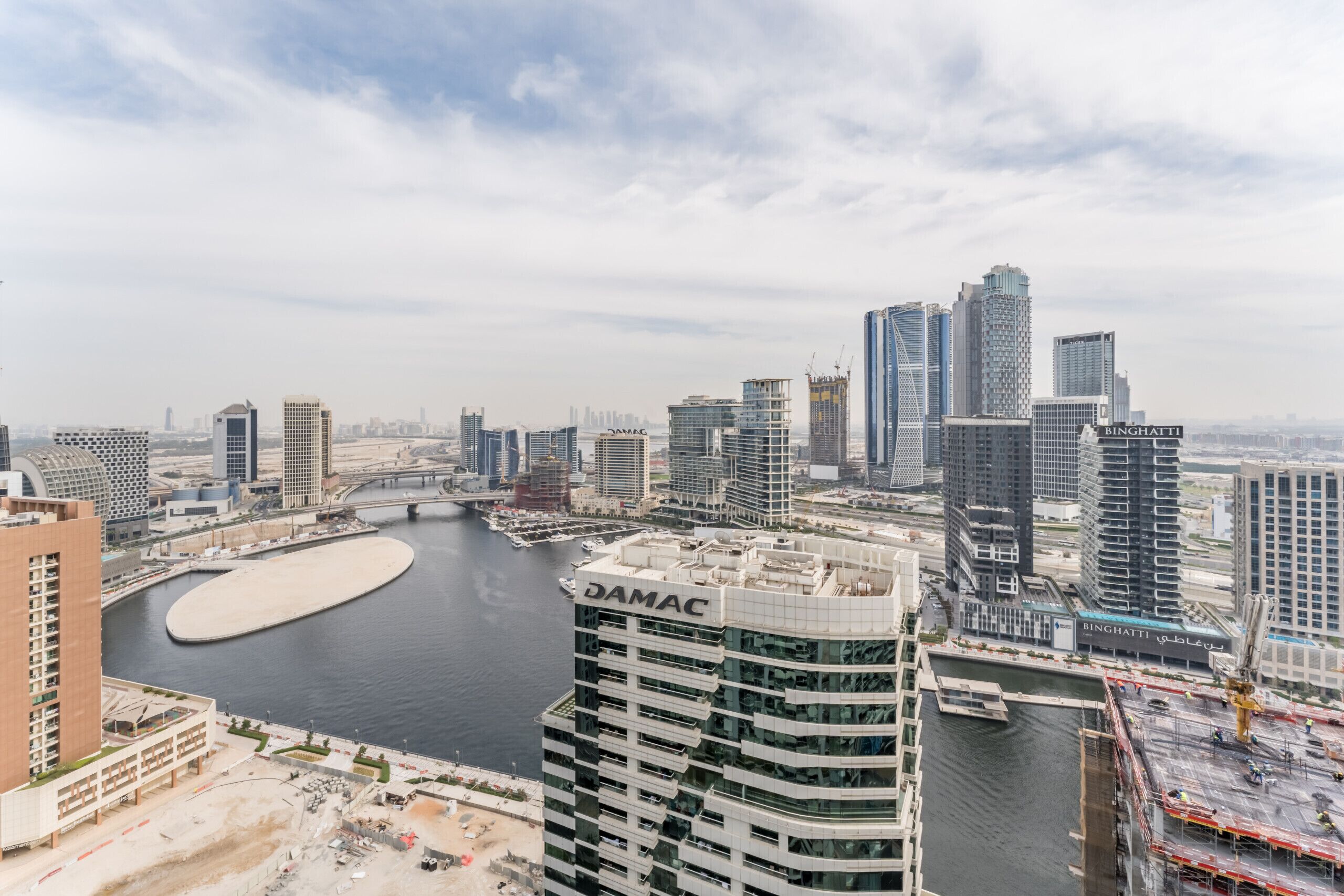 A high-rise building with a marina in the foreground and a bridge in the background.