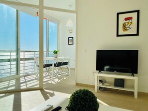 A modern living room with a large TV, a balcony with a view of the sea, and a dining area with a table and chairs. - Apartment in Torremolinos Near Playa Bajondillo (Torremolinos)