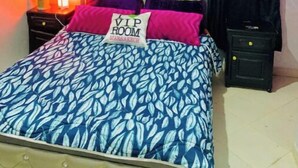 Un dormitorio con una cama, una mesita de noche, una lámpara y una cortina.