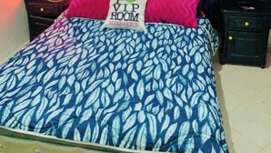 Una cama con colcha de hojas azules y blancas, cabecera capitonada y almohada con la inscripción 'VIP ROOM MARRAKECH'.