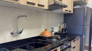 Una cocina moderna con armarios de madera, encimera negra, horno empotrado y refrigerador de acero inoxidable.