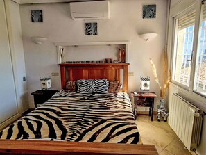 A bedroom with a zebra-striped bedspread, a wooden headboard, bedside tables with decorative items, a radiator, and a window with a view. - Casa Flamingo by Interhome (Calpe/Calp)