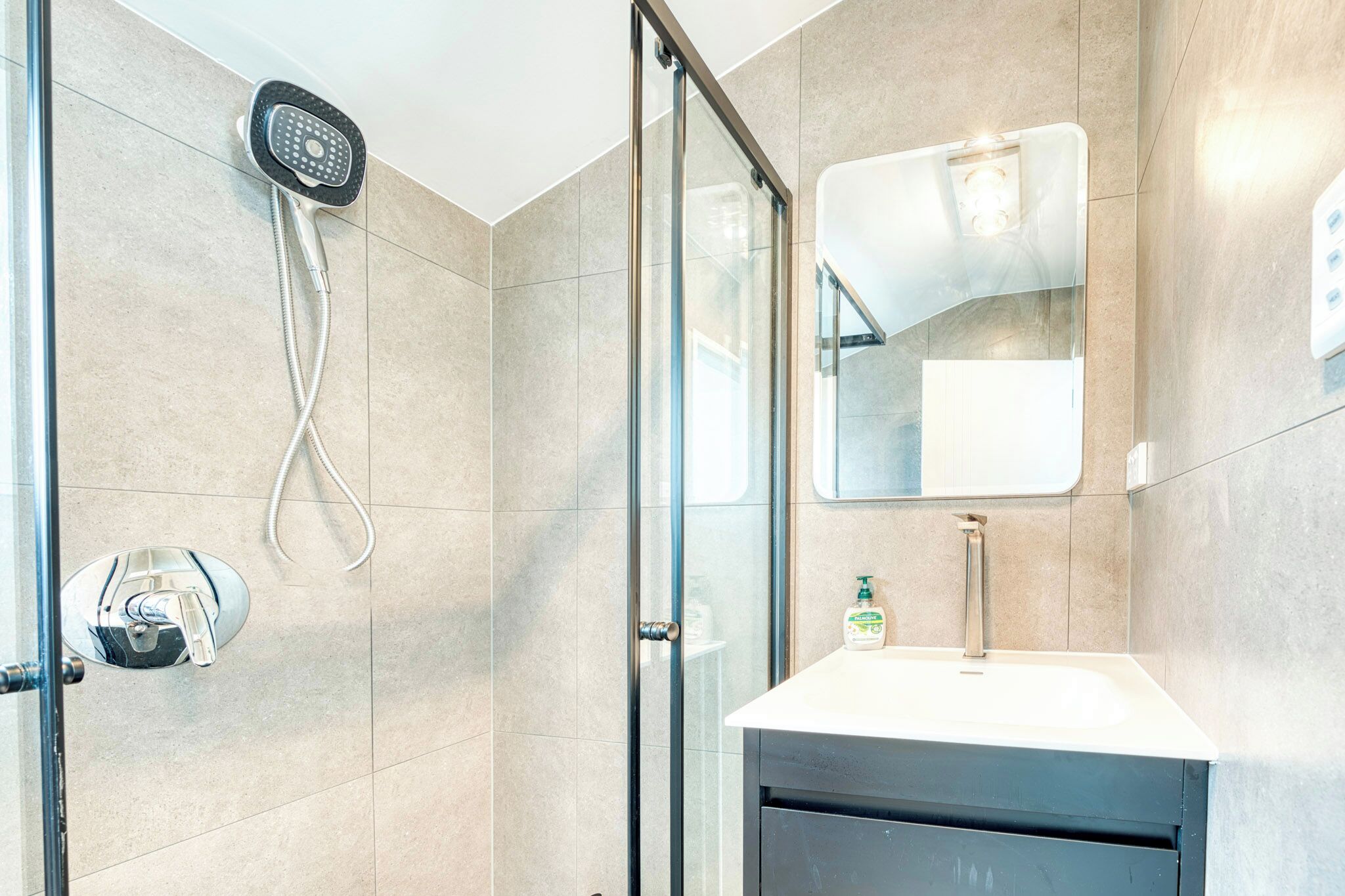 Une salle de bain moderne avec une douche à parois de verre, un lavabo avec un miroir et une douchette à main.