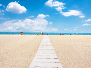 A beach with a clear sky, a paved walkway, and umbrellas. - für 3 Personen  + 1 Kind ca. 40 m² in Empuriabrava, Katalonien (Costa Brav by Interhome (Empuriabrava)