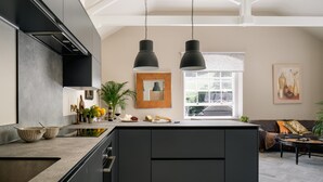 A modern kitchen with a large island, pendant lights, and a view to the living area. - Upper School House (Newton Abbot)