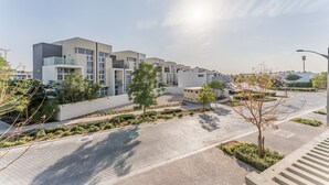 Un complexe résidentiel moderne doté d’une allée pavée, de jeunes arbres et d’un ciel dégagé.