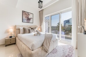 Un dormitorio moderno con una cama grande, una mesita de noche con lámpara, un cuadro en la pared y vistas al balcón exterior.