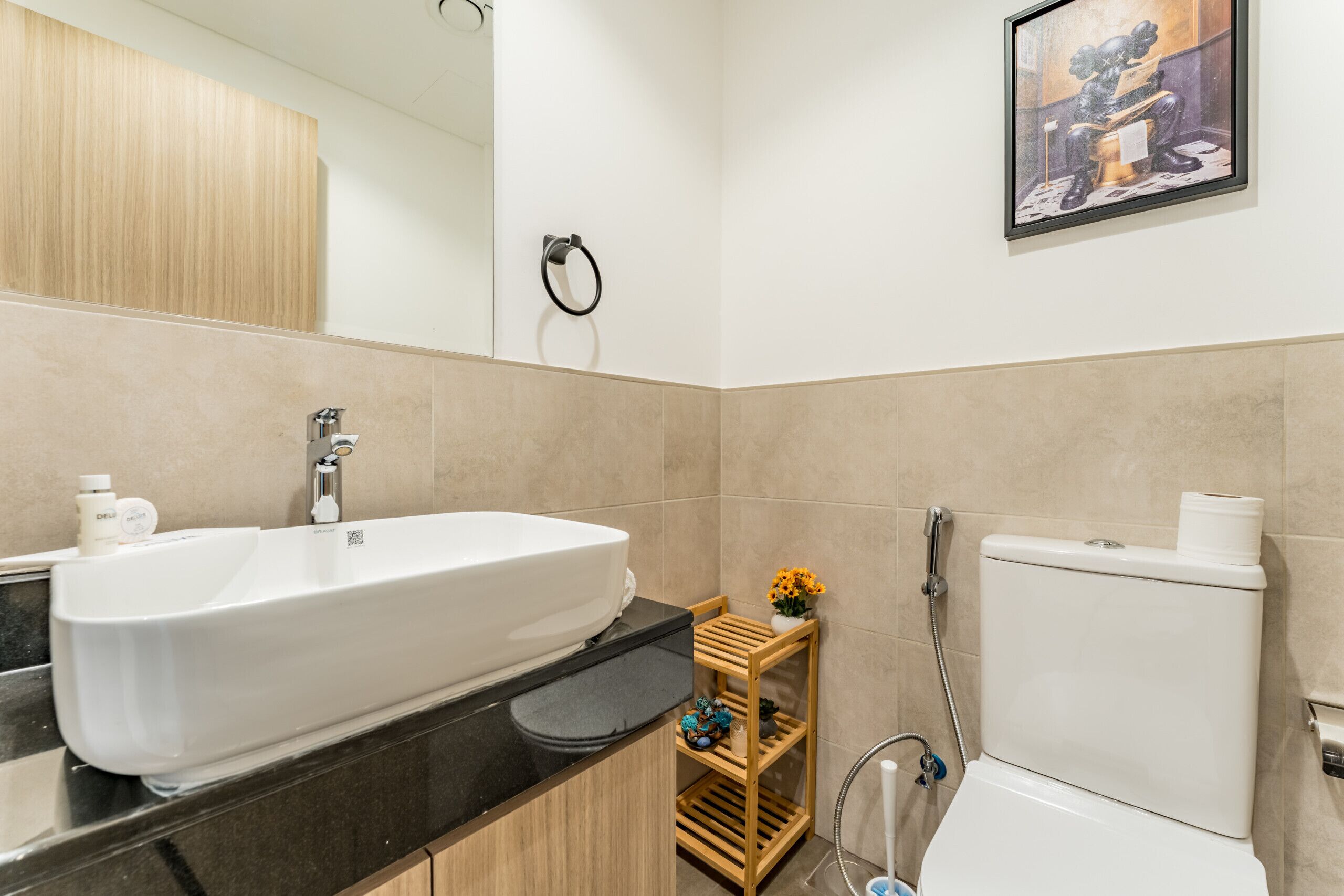Une salle de bain moderne avec un grand lavabo blanc, des toilettes et une étagère en bois où sont rangés les articles de toilette.
