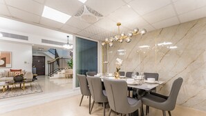 Un espace de salle à manger moderne avec un mur en marbre, un lustre et un escalier en arrière-plan.
