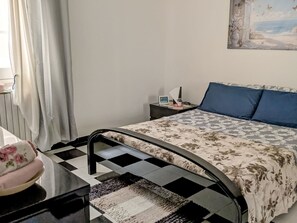 Ein Schlafzimmer mit Bett, Nachttisch, Lampe und einem Fenster mit Vorhängen.