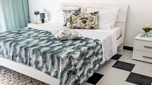 Una cama bien tendida con una colcha estampada, una mesita de noche con una lámpara y un pequeño florero con flores.