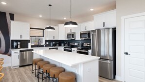 A modern kitchen with white cabinets, stainless steel appliances, a central island with bar stools, and pendant lighting. - Lazy River - Lake Views - Hot Tub - Pet Frndly! (Kimberling)