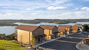 A row of wooden buildings with a parking lot and a lake in the background. - Lazy River - Lake Views - Hot Tub - Pet Frndly! (Kimberling)
