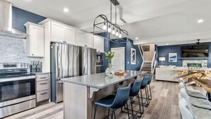 Una cocina moderna con electrodomésticos de acero inoxidable, una isla central con taburetes y un comedor con mesa y sillas de madera.