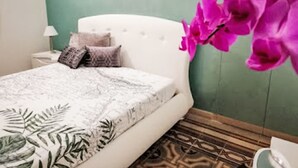 Camera da letto con un letto bianco, copriletto a motivi, cuscini, un comodino con una lampada e una parete verde.