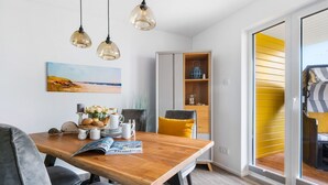 A dining area with a wooden table, grey upholstered chairs, a magazine, and a painting on the wall. - Vacation apartment "Dünengras" in the Baltic Sea resort of Olpenitz - Modern accommodation with a street (Kappeln)