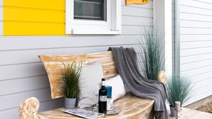 A wooden bench with a bottle of wine, a glass, and a candle on it. - Vacation apartment "Dünengras" in the Baltic Sea resort of Olpenitz - Modern accommodation with a street (Kappeln)