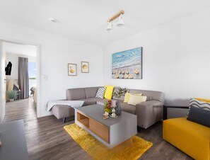 En moderne stue med en grå sofa, en gul lænestol og et sofabord. Væggene er prydet med billeder i rammer, og der hænger et maleri over sofaen.