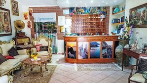 Een hotel lobby met een receptiebalie, een bank, een bijzettafeltje en een decoratieve wand met ingelijste foto's.