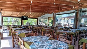 Een restaurant met houten tafels en stoelen, grote ramen en een houten plafond.