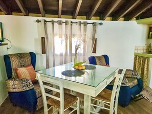 Een eethoek met een glazen tafel, blauwe fauteuils en een vaas met fruit op de tafel.