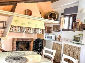 A kitchen with a brick fireplace, white chairs, a dining table, and a microwave. - Schöne Ferienwohnung in Iznájar mit Garten, Terrasse und Grill by Interhome (Fuentes de Cesna)