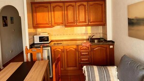 Una cocina compacta con armarios de madera, un microondas, un lavabo y una zona de comedor con mesa y sillas.