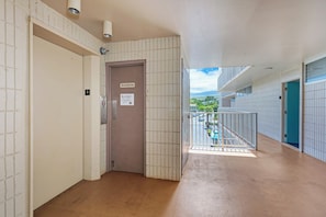 A corridor with a trash room door, a number 4 sign, and a view of a parking lot and greenery outside. - Kamaole Nalu 403 - Ocean View - New DESIGNER Remodel wA/C (Kihei)