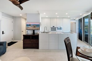A modern kitchen with a central island, built-in appliances, and a large window offering a view. - Kamaole Nalu 403 - Ocean View - New DESIGNER Remodel wA/C (Kihei)