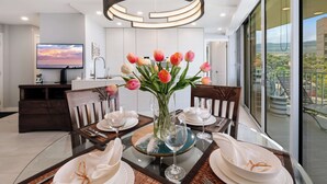 A modern dining area with a glass table, chairs, and a vase of tulips. - Kamaole Nalu 403 - Ocean View - New DESIGNER Remodel wA/C (Kihei)