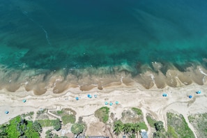 An aerial view of a beach with clear turquoise water, sandy shore, and scattered umbrellas. - Kamaole Nalu 403 - Ocean View - New DESIGNER Remodel wA/C (Kihei)