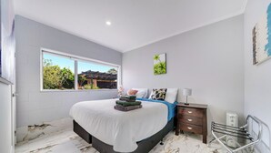 Une chambre à coucher comprenant un lit, une table de chevet, une lampe, un radiateur et une fenêtre donnant sur un paysage verdoyant.