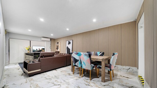Un salon moderne avec un canapé d’angle, une table à manger avec des chaises et un sol en marbre.