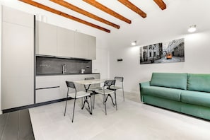 A modern kitchen with white cabinets and a black countertop, a dining area with a table and chairs, and a green sofa. - Alessia's Flat - Naviglio Grande (Buccinasco)
