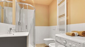 Egy modern fürdőszoba zuhanyzóval, WC-vel és mosógéppel.