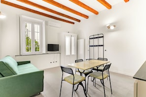 A modern living room with a green sofa, a wooden dining table with four chairs, a TV, and a wardrobe. - Alessia's Flat - Naviglio Grande (Buccinasco)