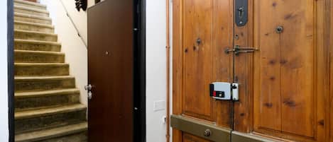 A wooden door with a metal handle and a lock, a staircase with a handrail, and a wall-mounted light switch.