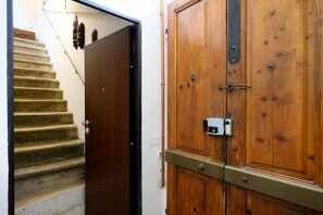 A wooden door with a metal handle and a lock, a staircase with a handrail, and a wall-mounted light switch. - Cozynest in Florence  (Firenze)