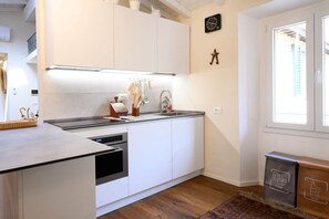 A modern kitchen with white cabinetry, a built-in oven, and a stainless steel sink. There is a clock on the wall and a trash bin with recycling symbols. - Cozynest in Florence  (Firenze)