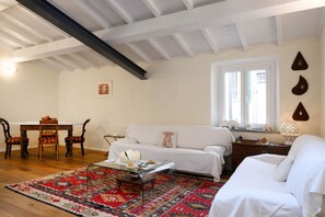 A room with a white sofa, a dining table with chairs, a patterned rug, and a window with curtains. - Cozynest in Florence  (Firenze)