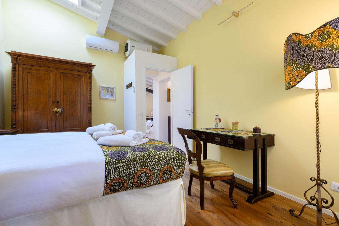 A bedroom with a bed, a wooden wardrobe, a desk with a lamp, and a chair.