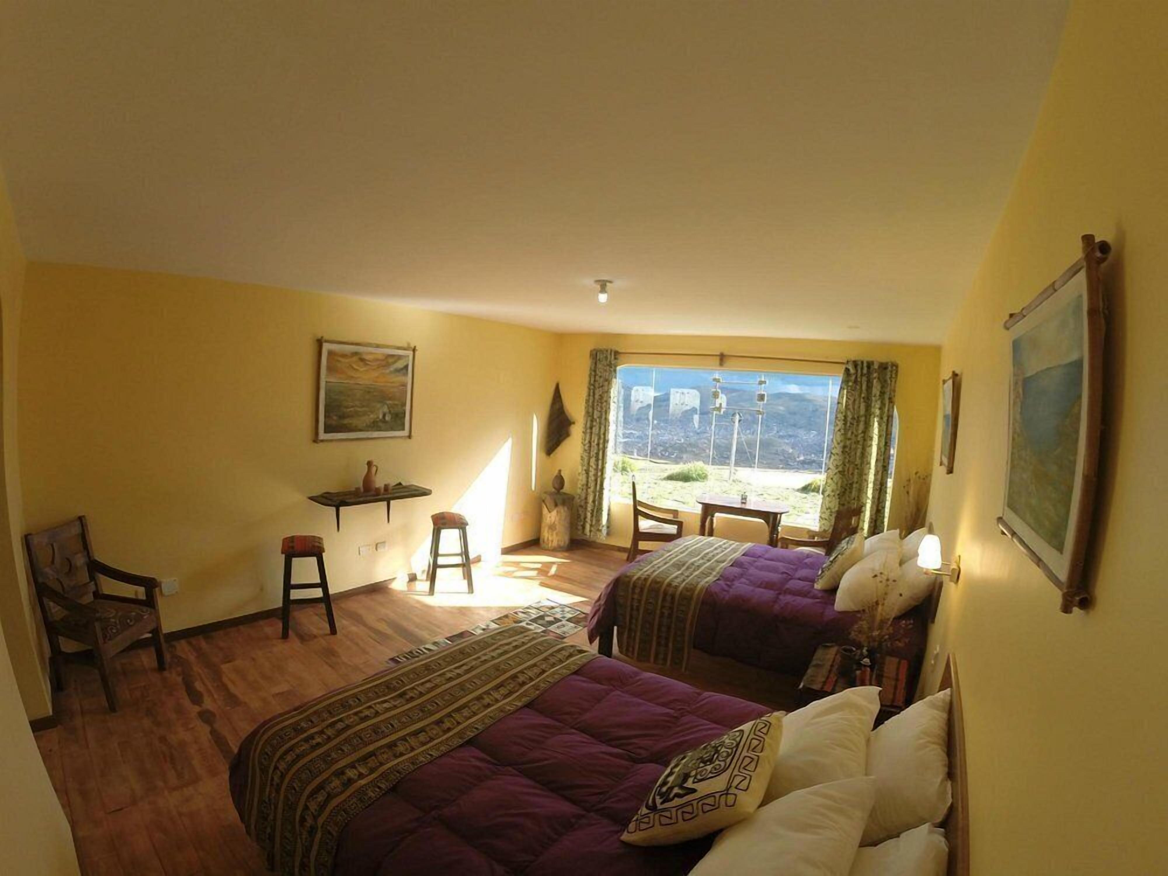 Una habitación con dos camas, una mesita, una silla y una ventana con vistas.