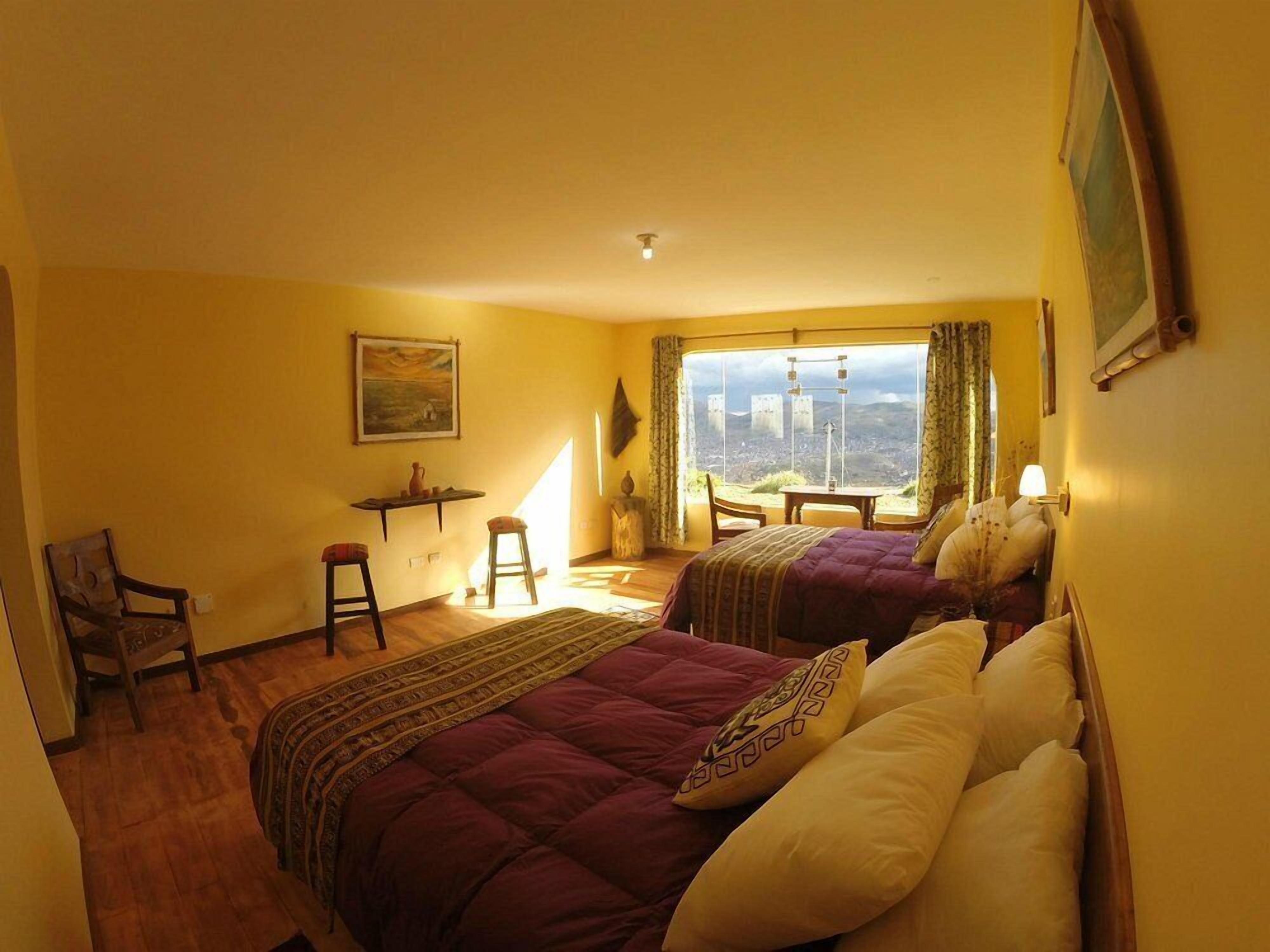Quarto de hotel com duas camas, uma escrivaninha, uma cadeira e vista para a paisagem urbana.
