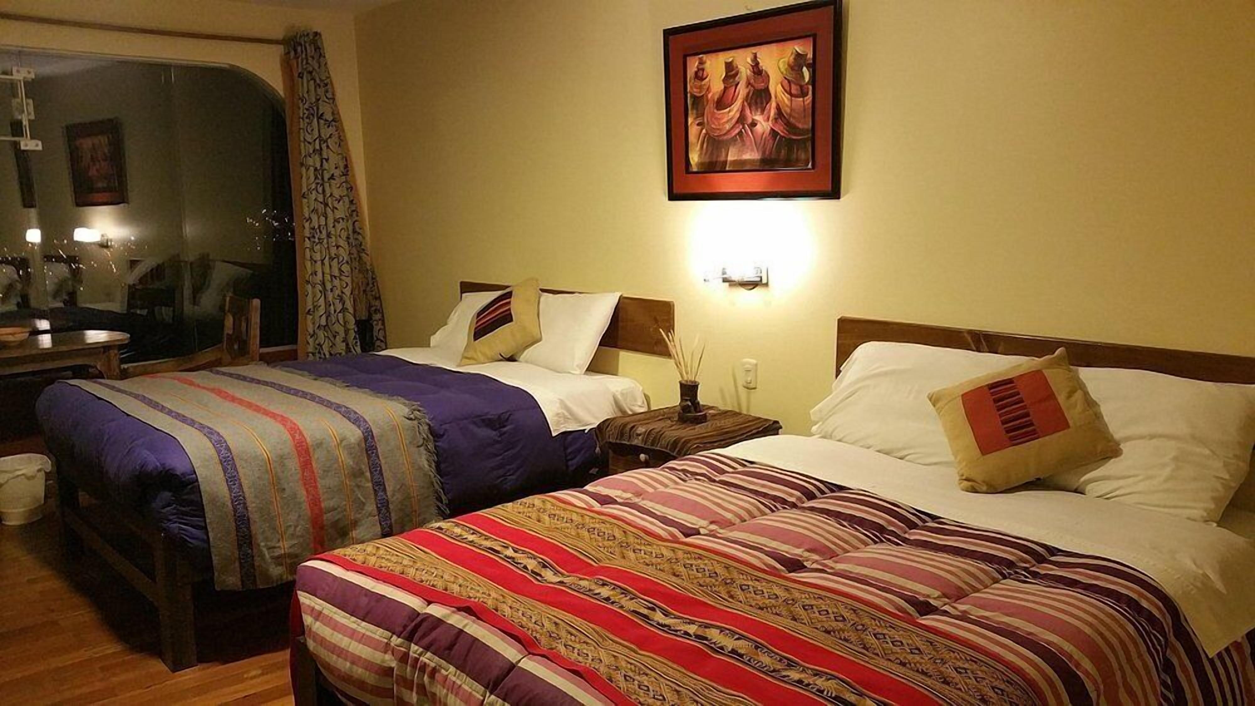 A hotel room with two beds, each with striped bedding, a nightstand, a wall-mounted lamp, and a framed picture above the beds.