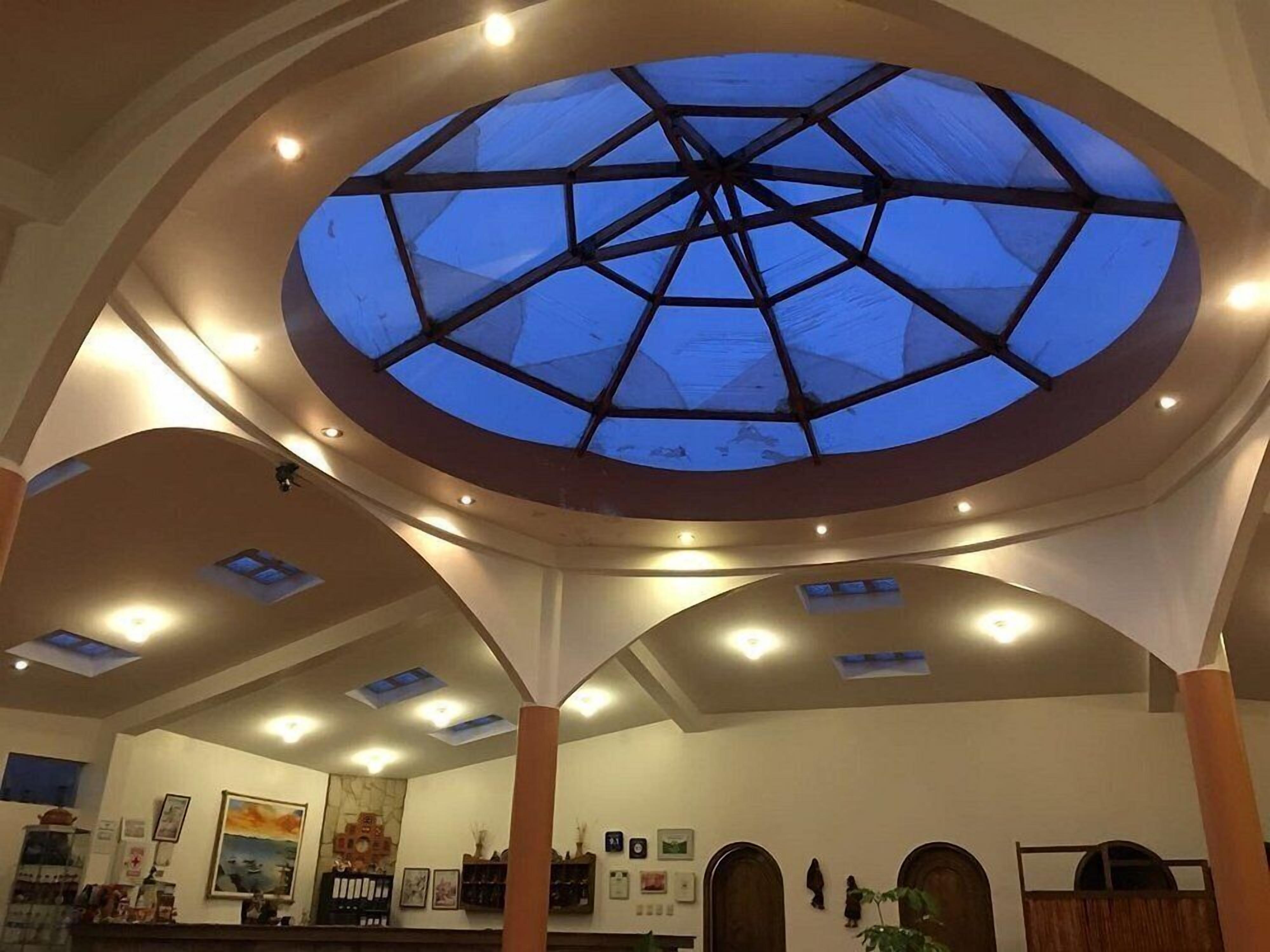 A hotel lobby with a large skylight, multiple ceiling lights, and a reception desk.