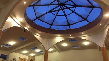 A hotel lobby with a large skylight, multiple ceiling lights, and a reception desk.