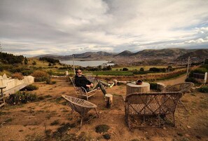 A person relaxing on a wicker chair with a scenic view of a lake and mountains in the background.