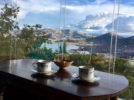 Una mesa con dos tazas y un cuenco, con vistas a un paisaje montañoso con un lago y una ciudad a lo lejos.