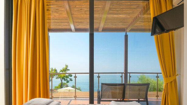 A balcony with a bed, yellow curtains, and a TV. - Kalma Villa Tria in Moudania (Nea Propontida)