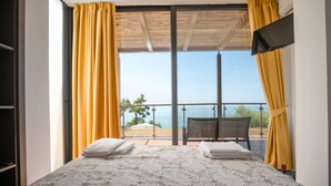 A hotel room with a bed, two towels, a chair, and a view of the sea through large windows. - Kalma Villa Tria in Moudania (Nea Propontida)